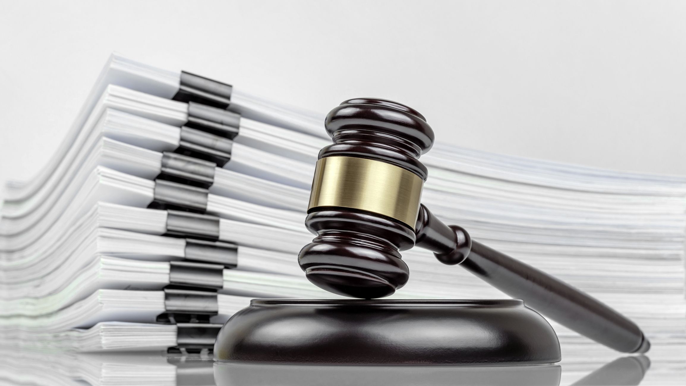 Close-up of a judge's gavel and a stack of court files and documents on a desk.